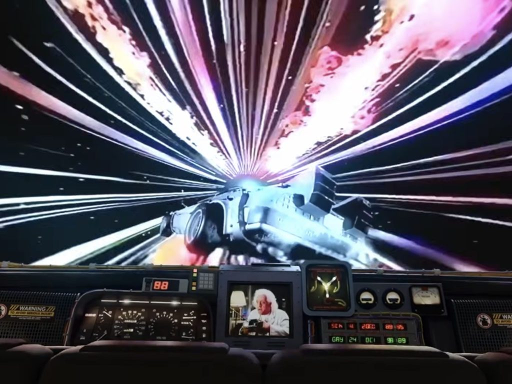 Screen grab from Back to the Future: The Ride at Universal Studios Florida, showing the DeLorean traveling through a time-warp sequence with Doc Brown visible on the ride vehicle monitor.