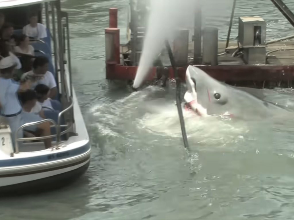 Animatronic shark surfacing beside an Amity boat during JAWS at Universal Studios Florida, with a water cannon spraying behind it.