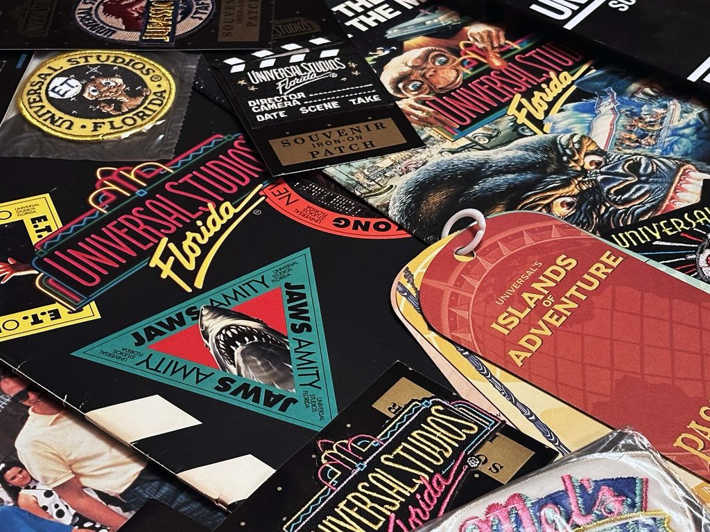 Collection of vintage Universal Studios Florida souvenirs and memorabilia, including JAWS, E.T., Kongfrontation, and Islands of Adventure patches and printed items.