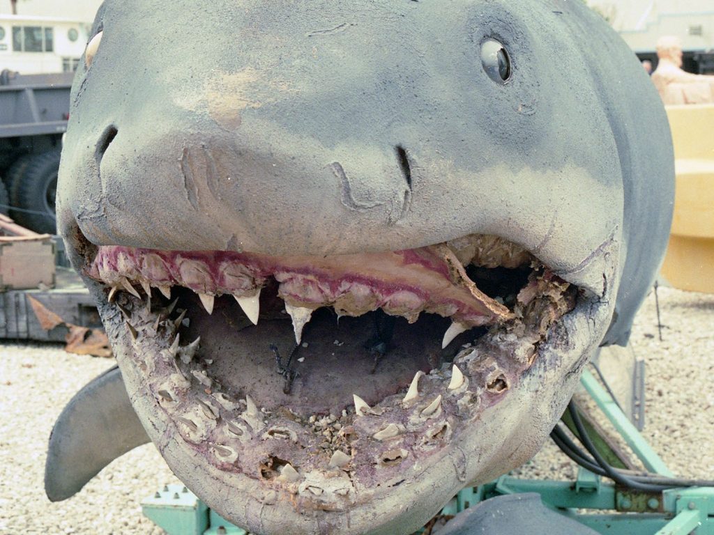 Jaws: The Revenge shark on display in the Universal Studios Florida Boneyard, showing severe deterioration around the mouth and missing teeth.