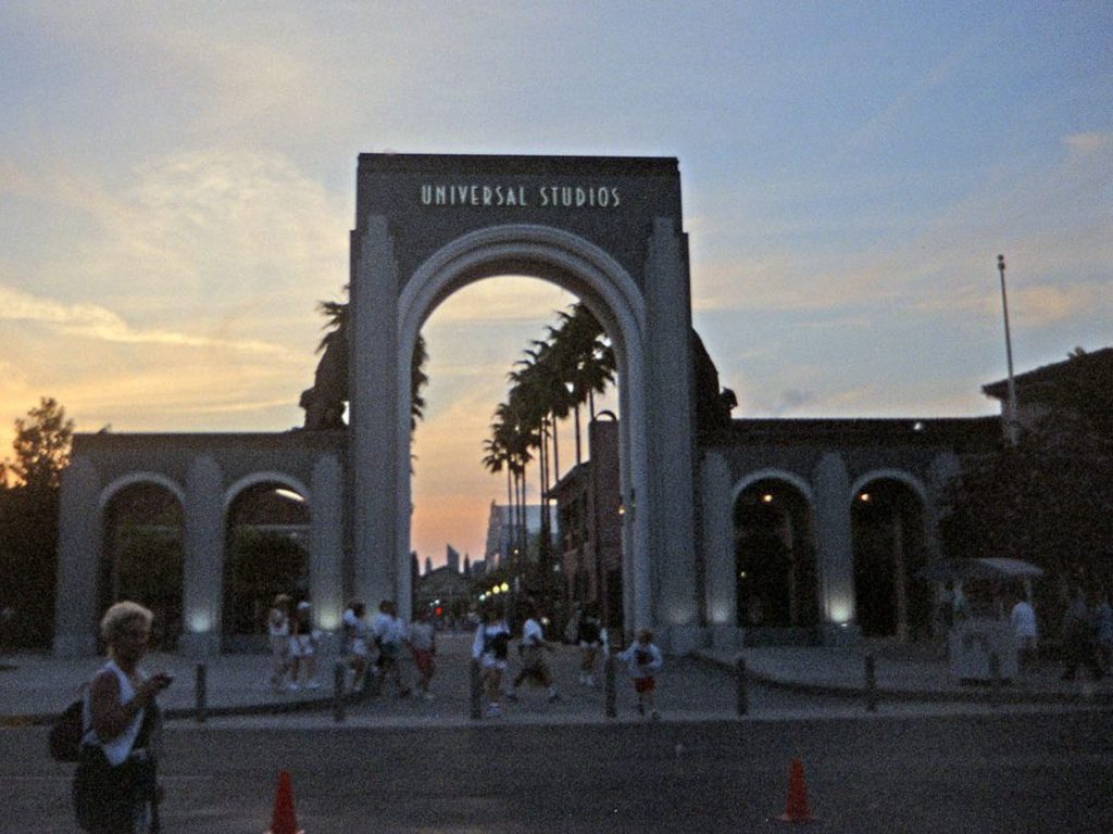 Original Universal Studios Florida entrance arches at sunset, with guests walking beneath the main arch into the park.